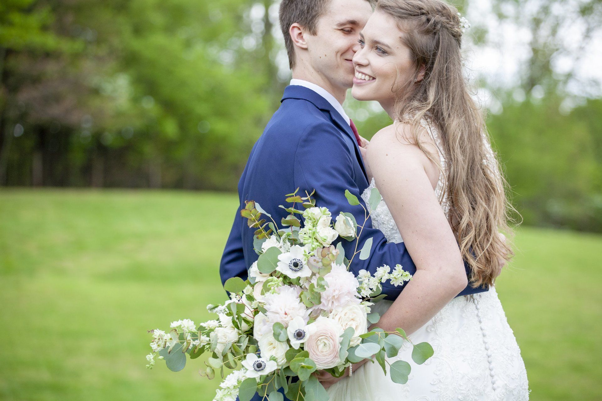 Couple embracing outdoors, bride holding a white bouquet in a green park
