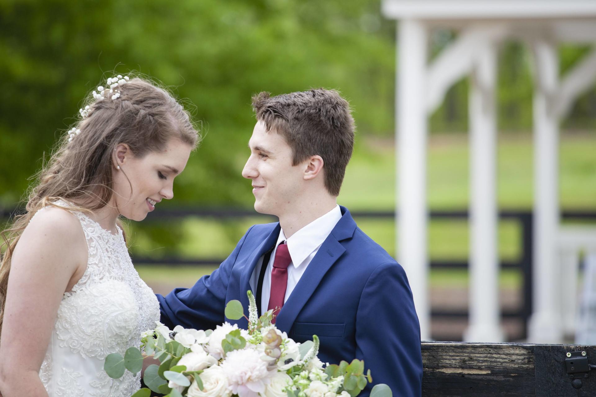 Bride and groom smiling at each other outdoors, holding a bouquet at their wedding ceremony