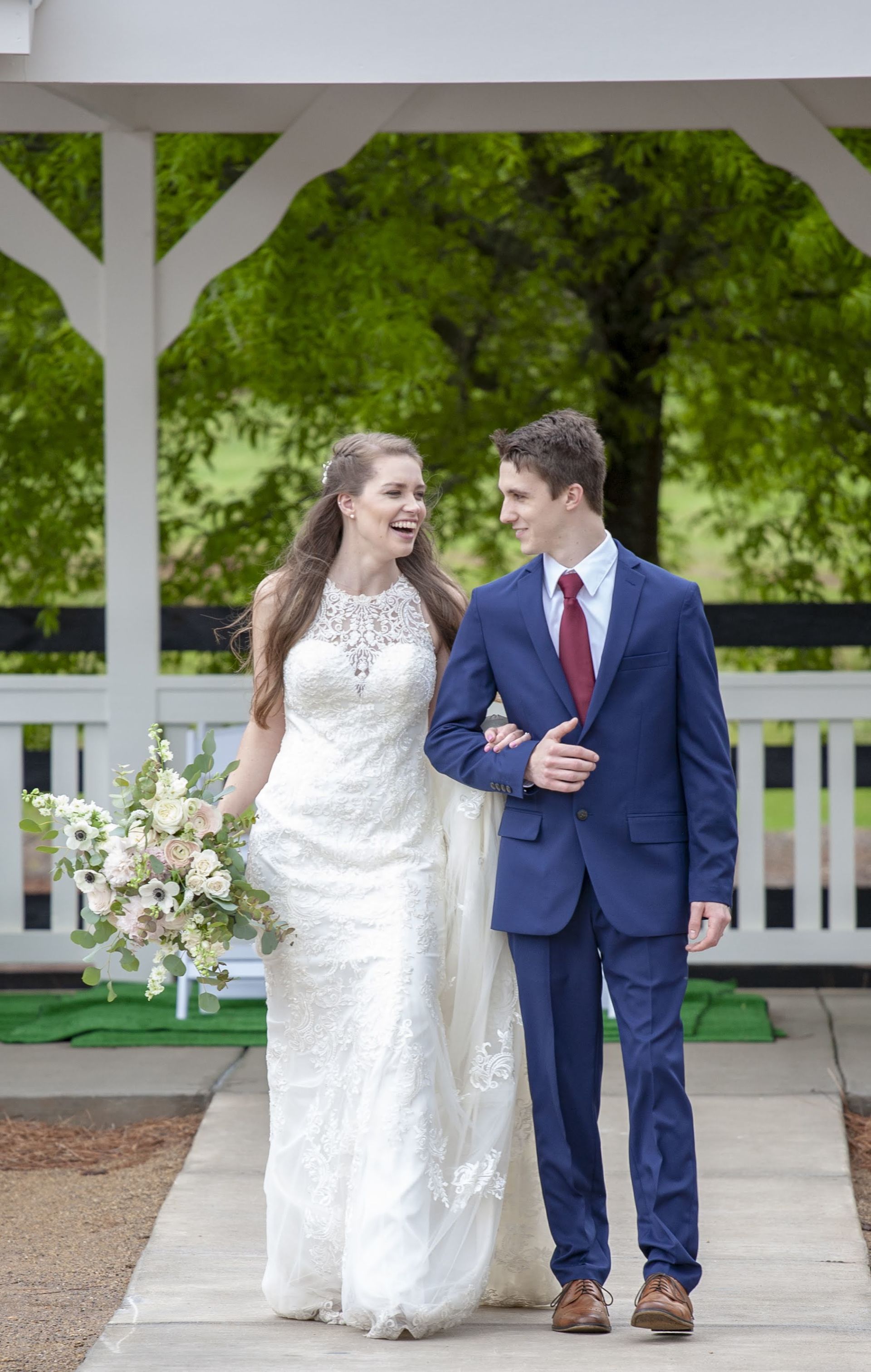 Bride and groom walking together under a gazebo, smiling at each other in wedding attire.