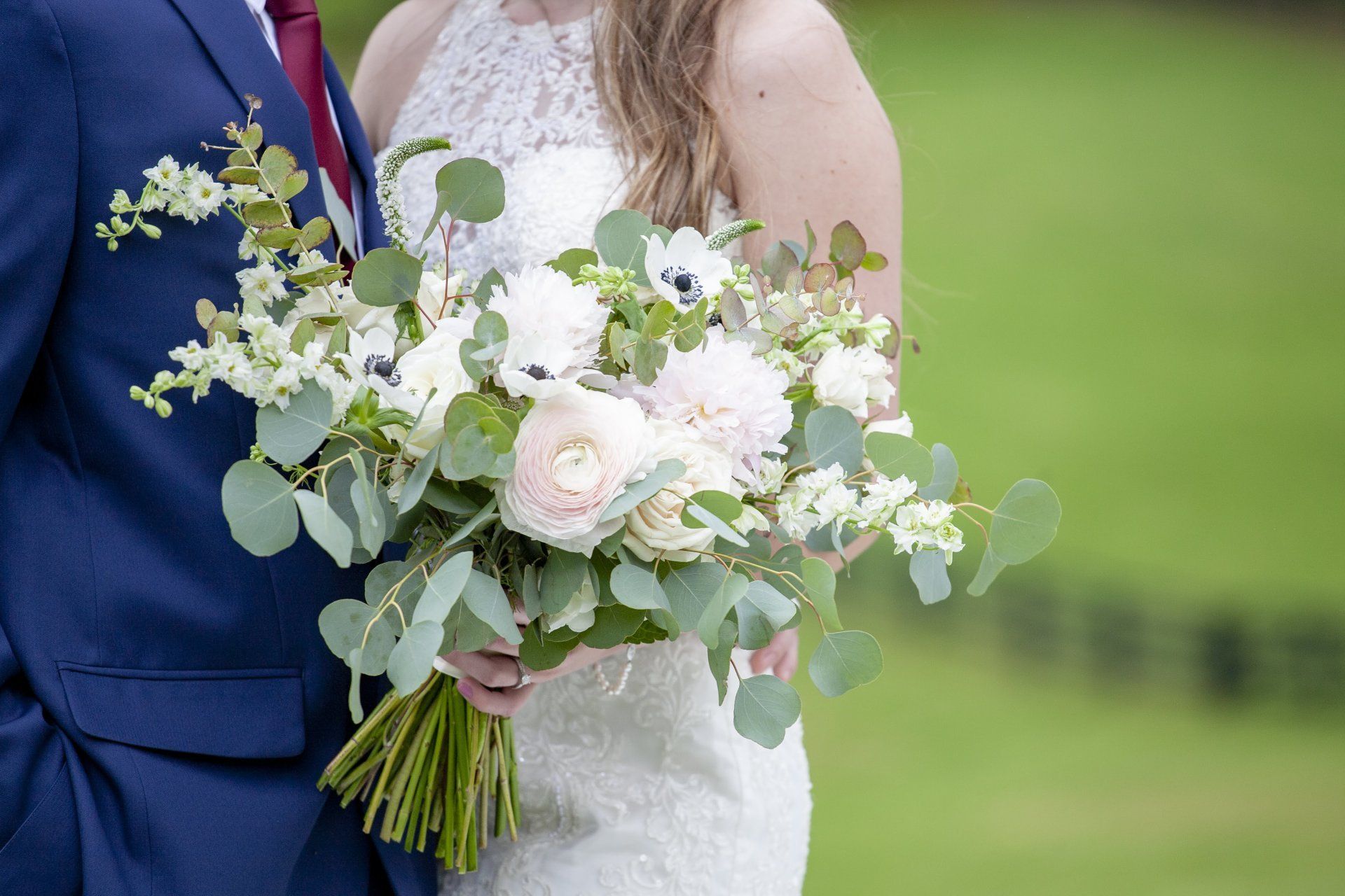 Bride and groom holding a white-and-green wedding bouquet outdoors