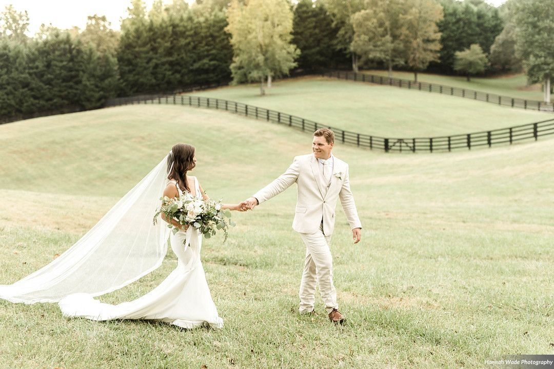 A bride and groom are walking in a field holding hands.