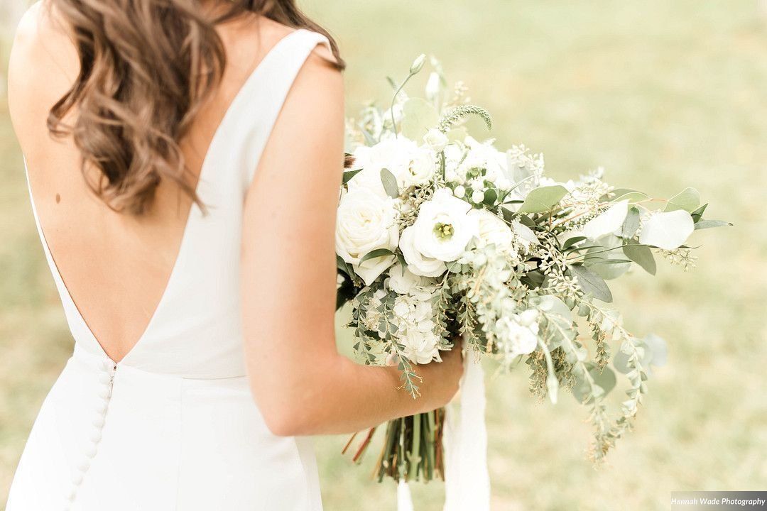 A bride in a white dress is holding a bouquet of white flowers.