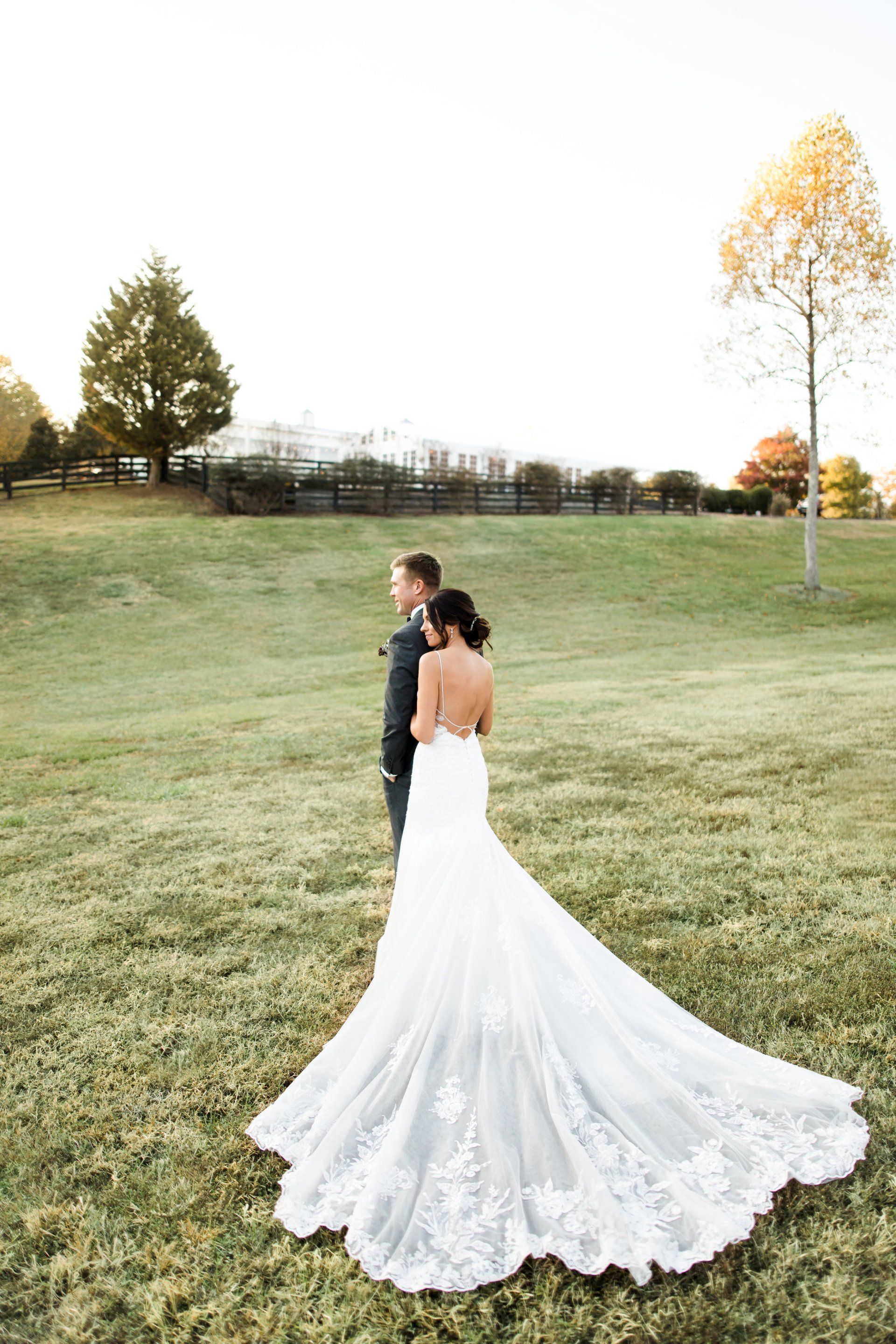 A bride and groom are standing in a grassy field . the bride is wearing a long wedding dress.