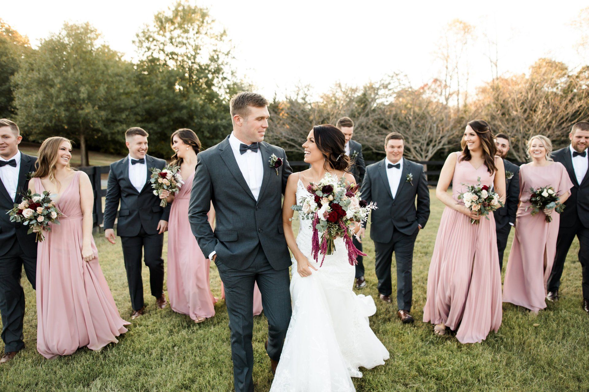 Bride and groom walking with their wedding party in a field.
