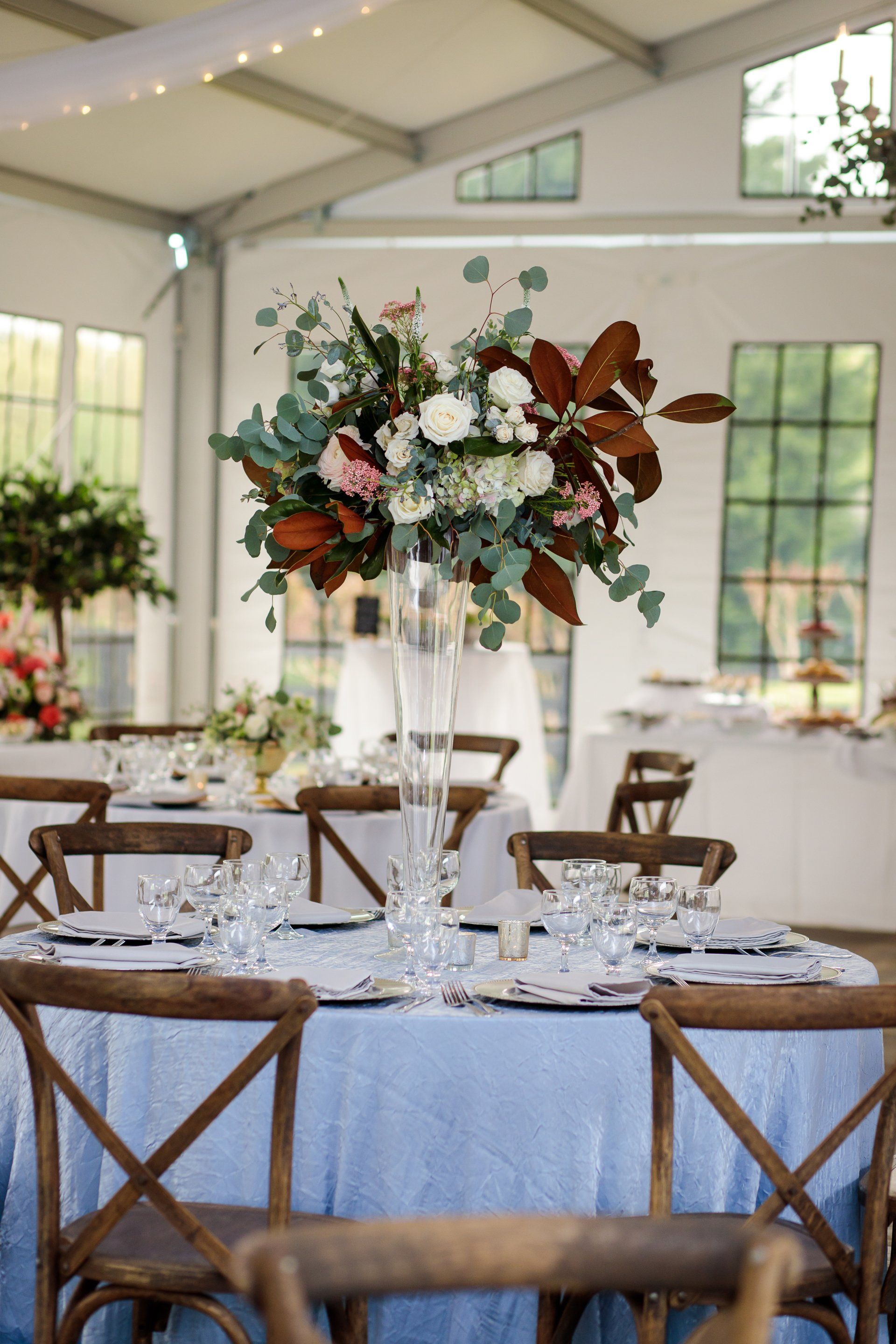 Elegant wedding reception table with white floral centerpiece and blue tablecloth in a bright tented venue