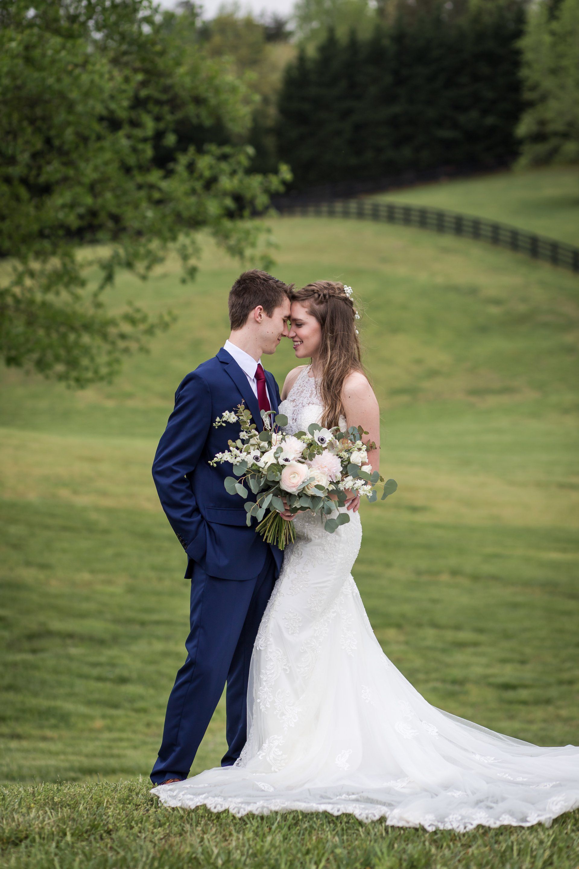 Bride and groom kissing outdoors in a green field, holding a bouquet