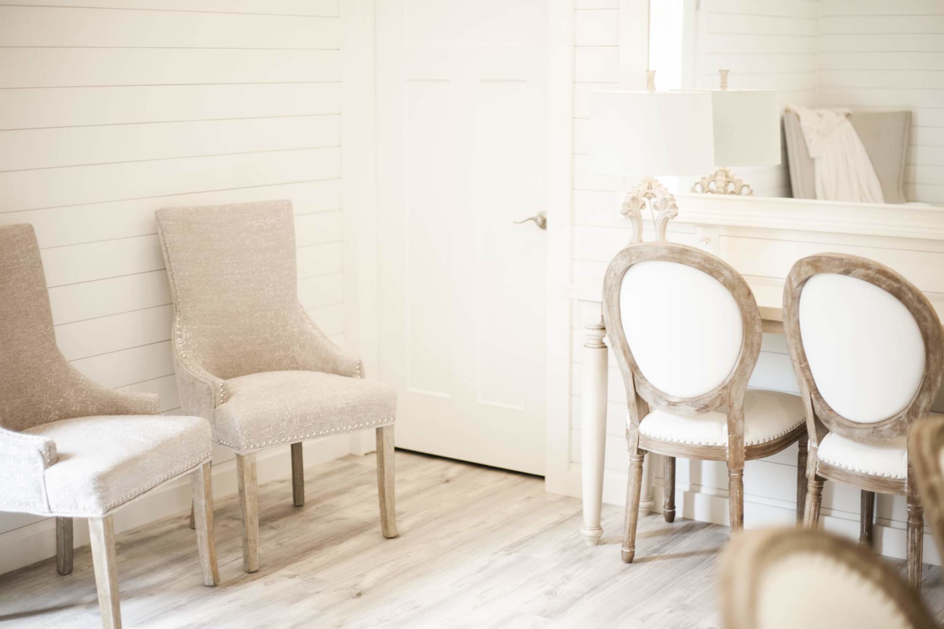 Bright white dining room with two beige chairs and a round table by a sunlit door