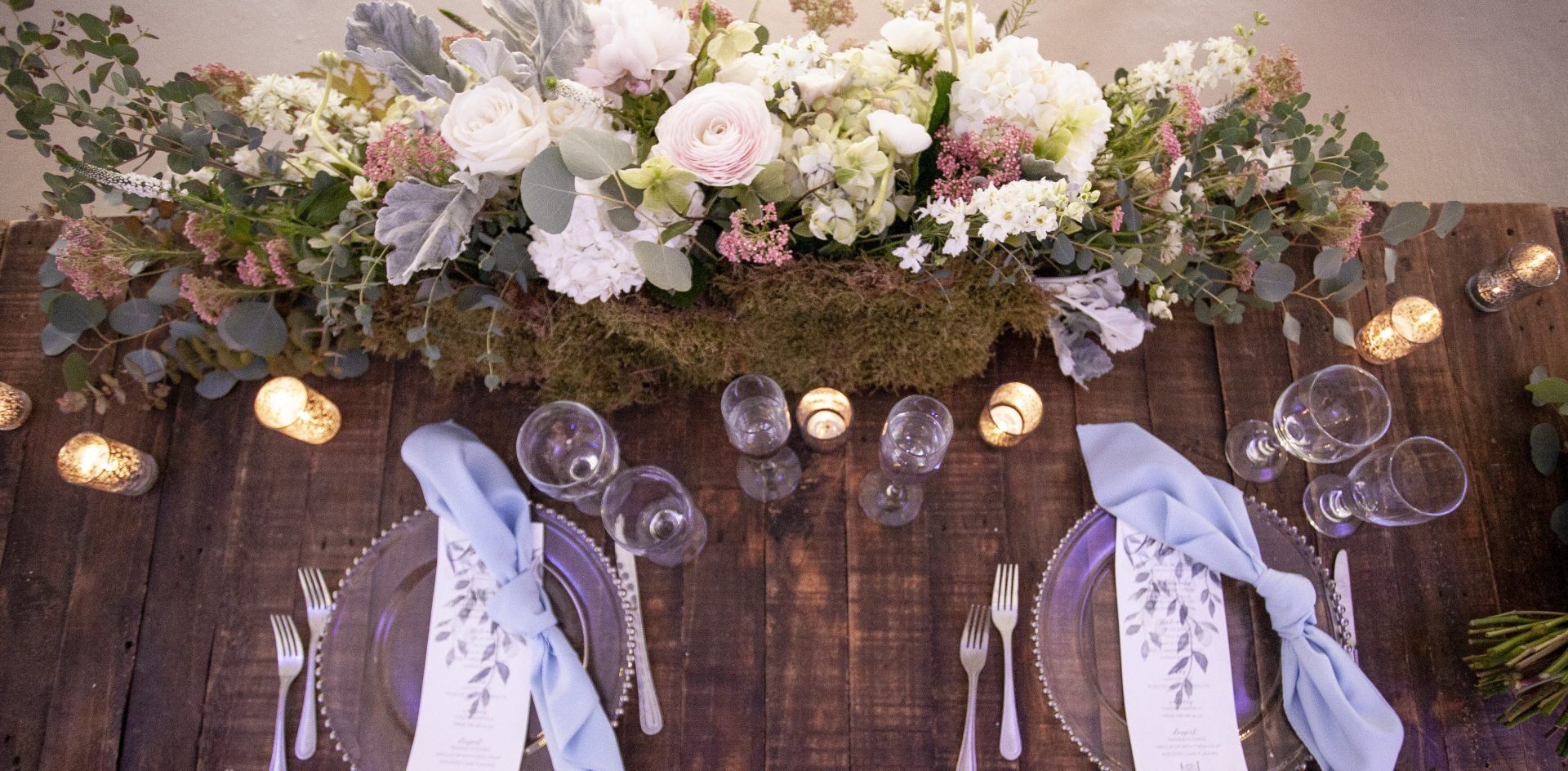 Elegant floral wedding reception table with white place settings and soft candlelight