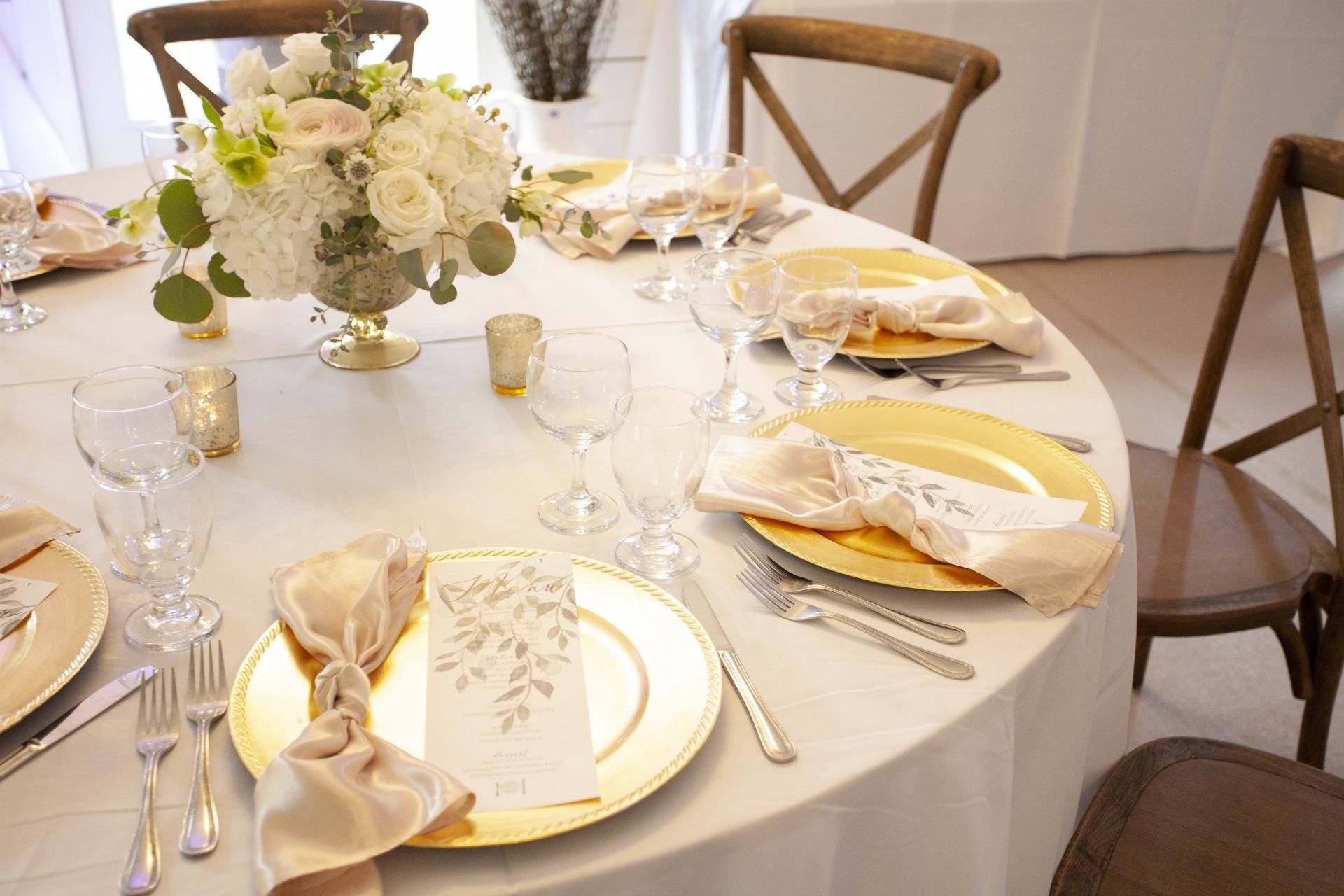 Elegant round dining table set with white and gold place settings and floral centerpiece