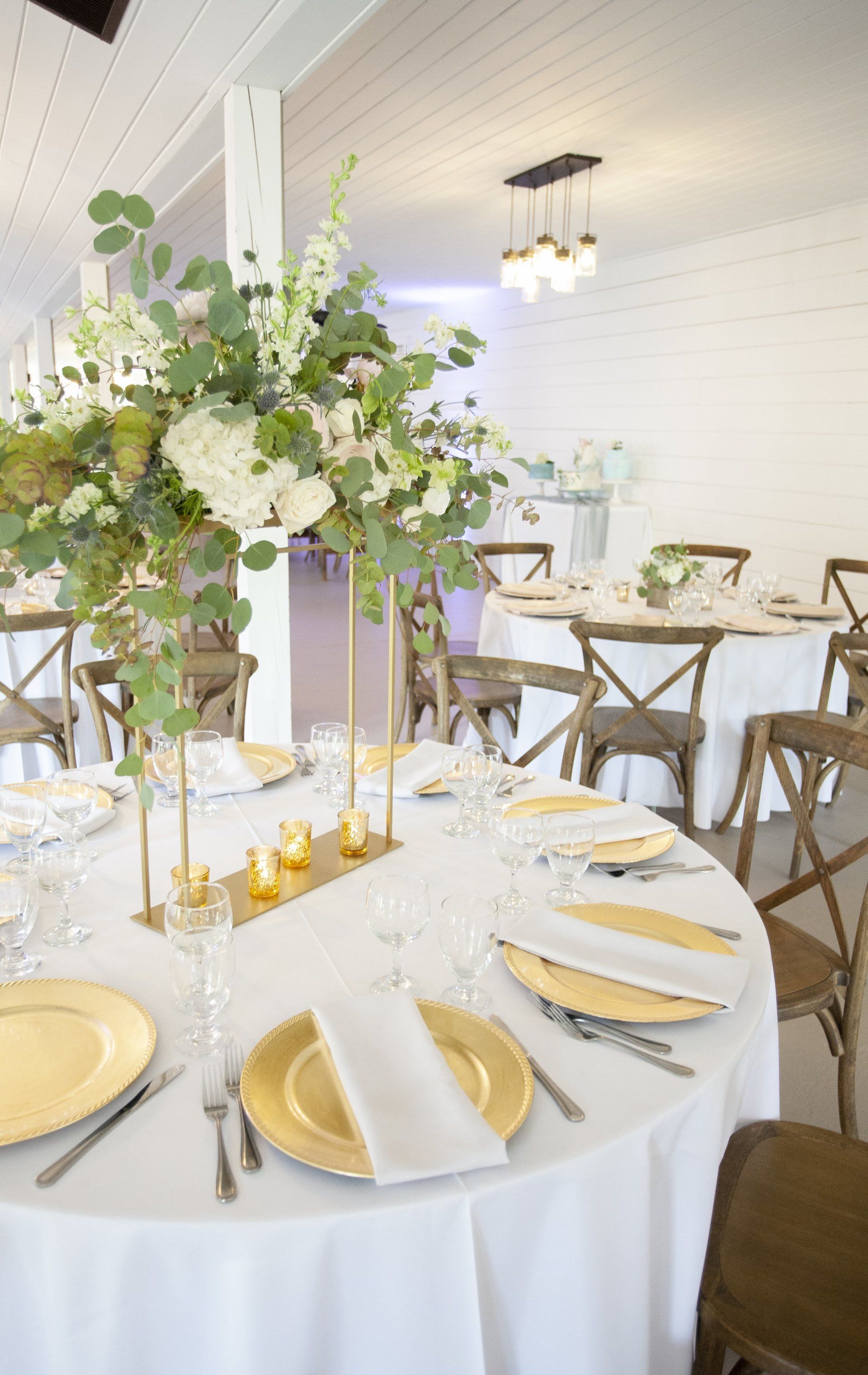 Elegant white banquet table with gold accents and floral centerpiece in a bright reception room