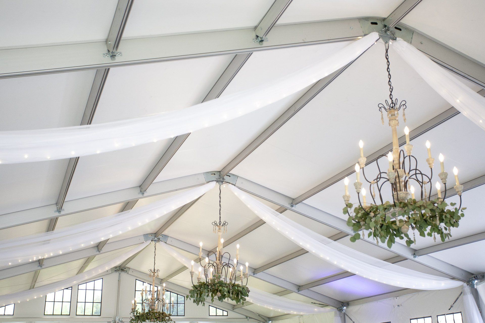 Chandelier-lit tent ceiling with white draped fabric and exposed beams