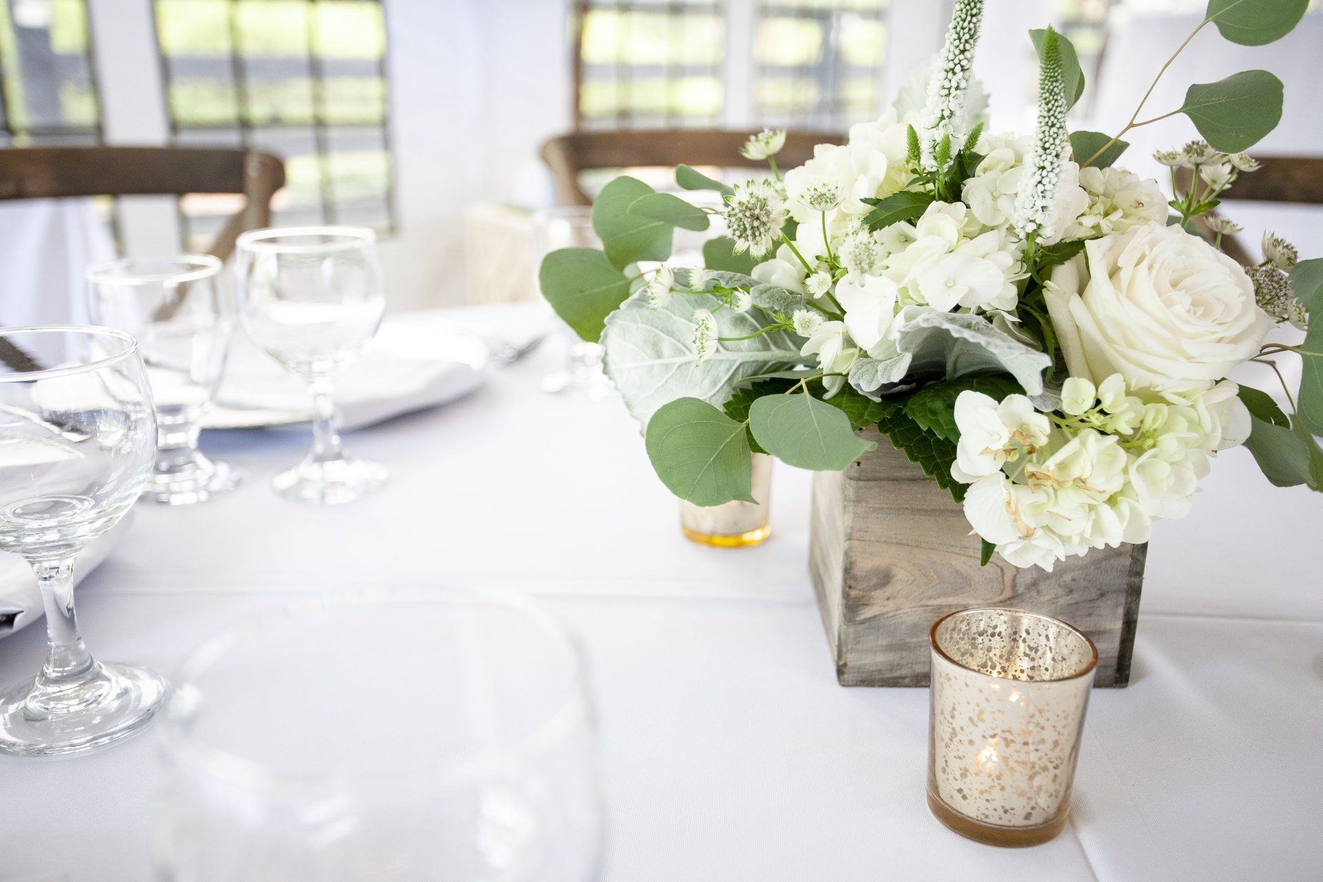 White floral centerpiece on a set dining table with glassware and votive candle