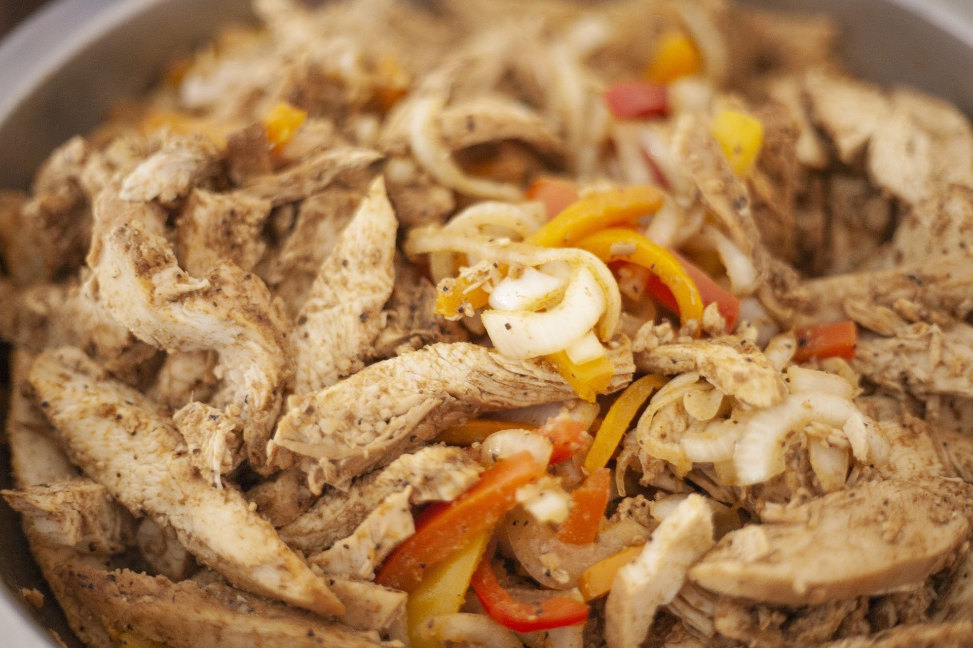 Close-up of shredded chicken with onions and red peppers in a pan