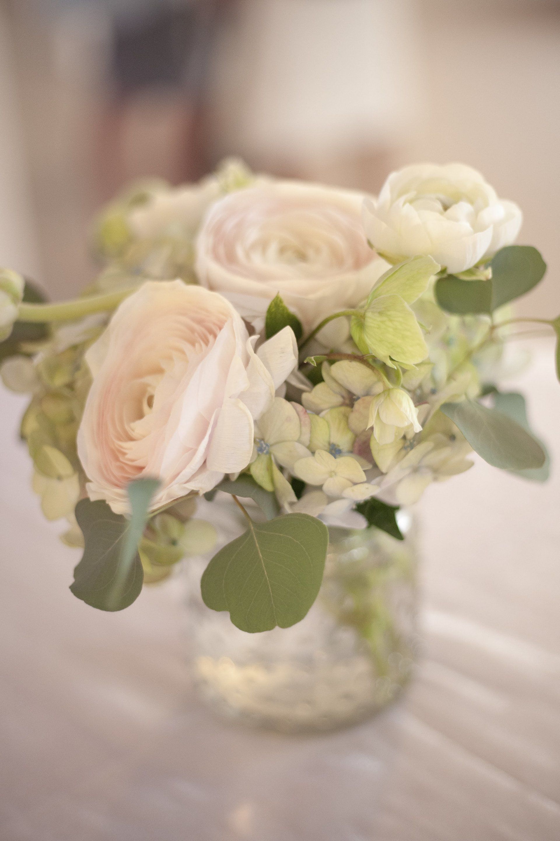 Soft blush roses and white flowers in a clear glass vase on a table.