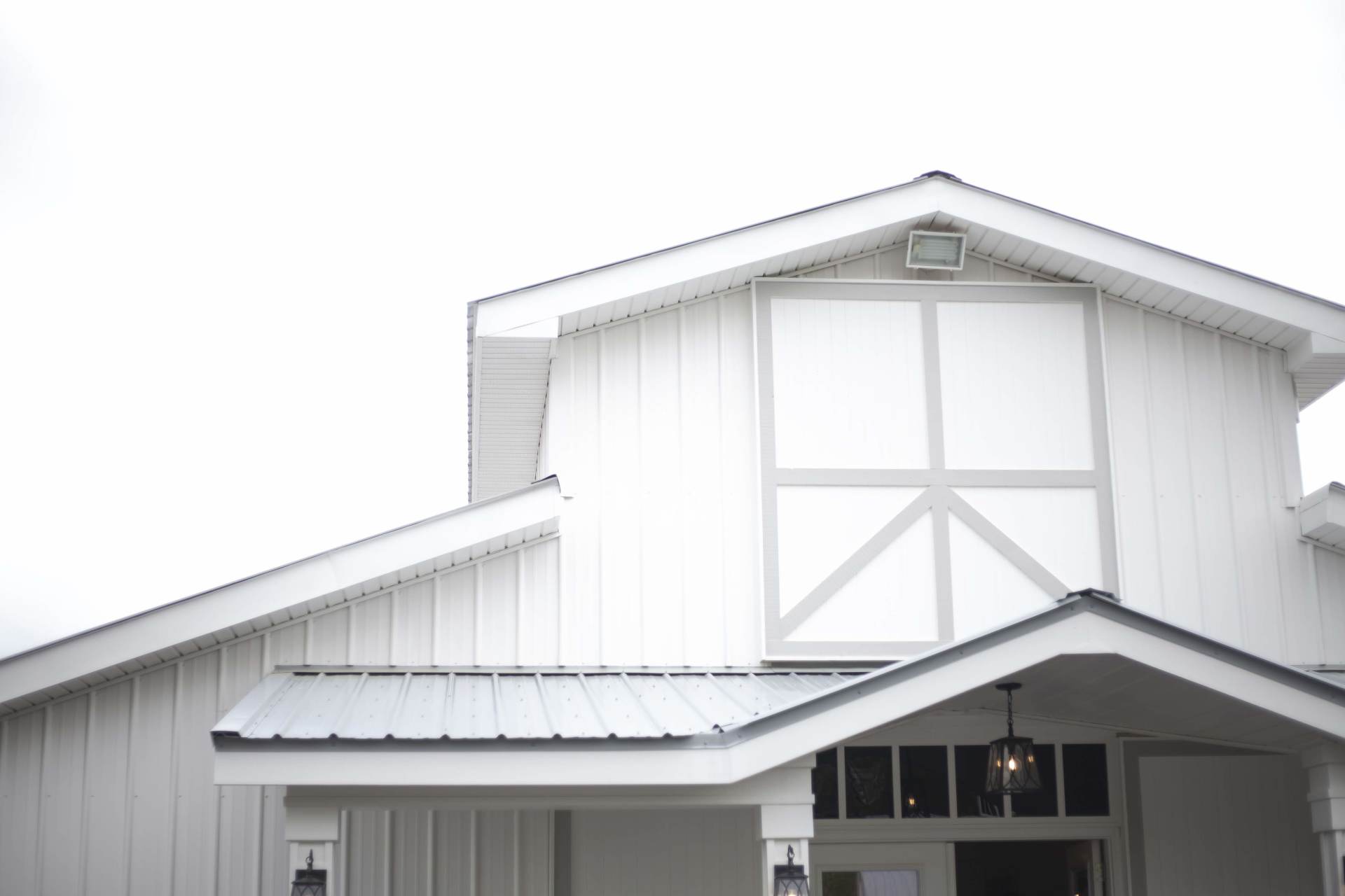 White barn exterior with a gray metal roof and large upper window above the entrance