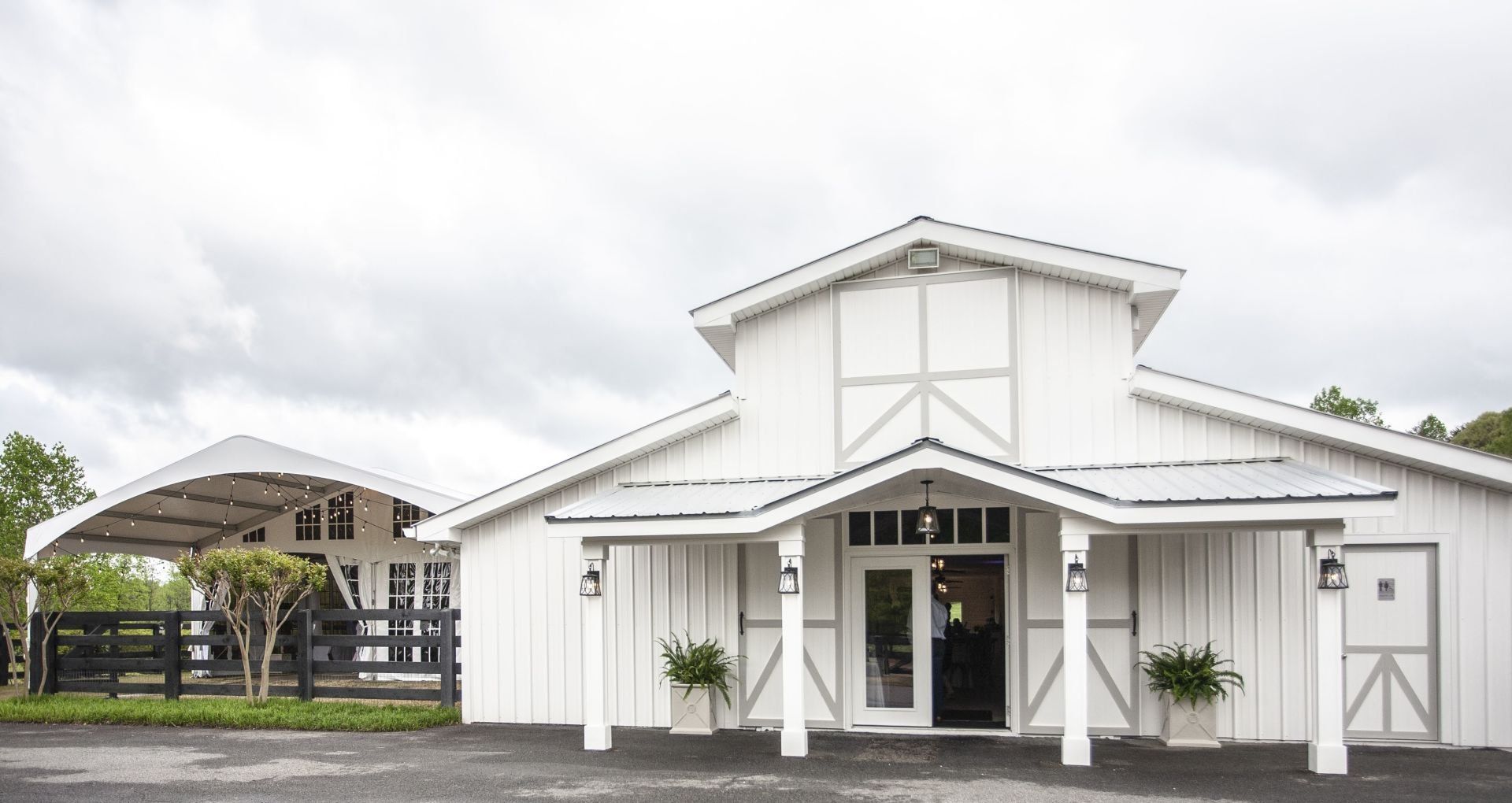 White barn-style event hall with a covered entrance and open pavilion on the left under a cloudy sky