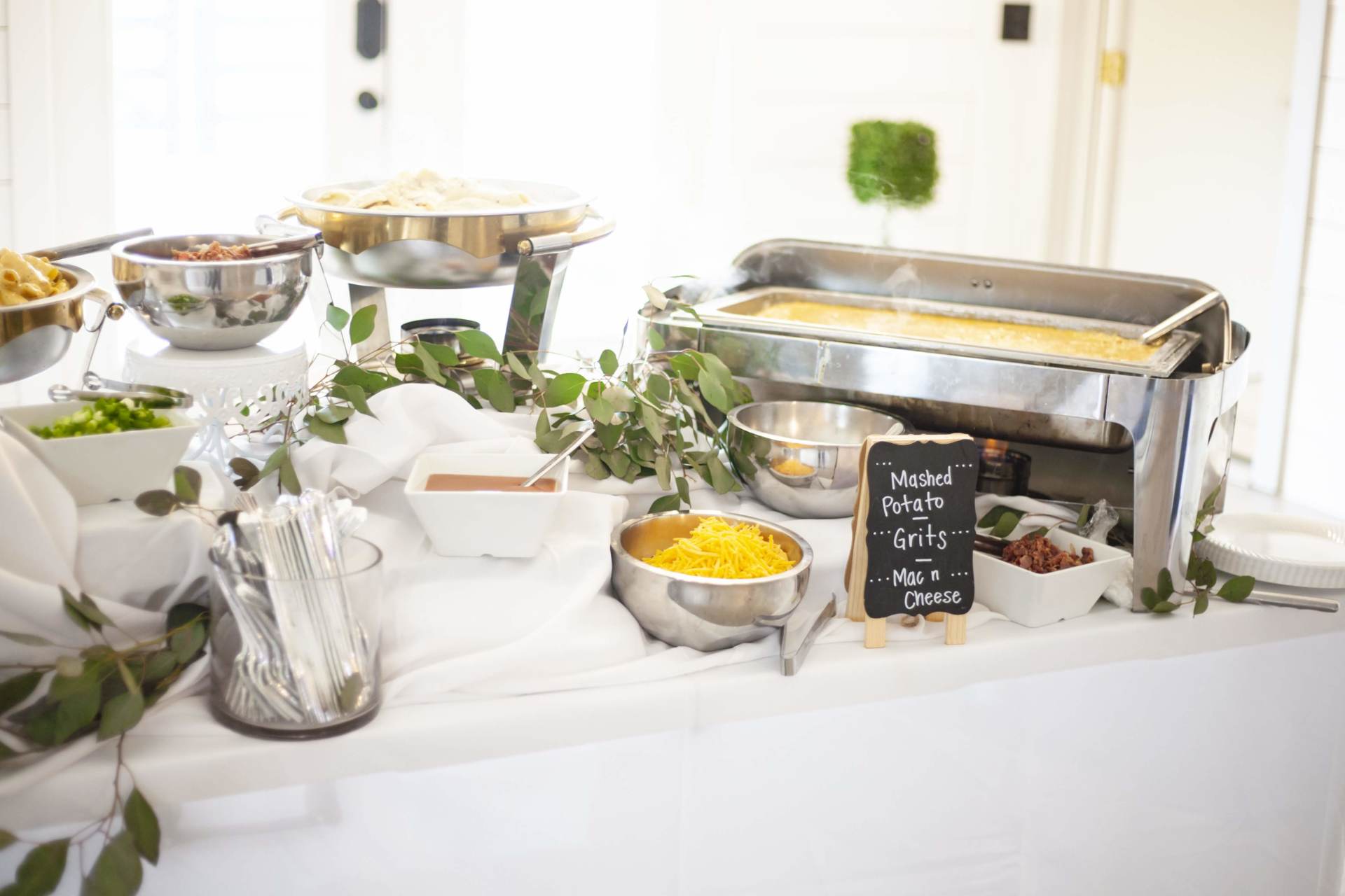 Buffet table with chafing dishes, salad bowls, and fresh herbs on a white tablecloth