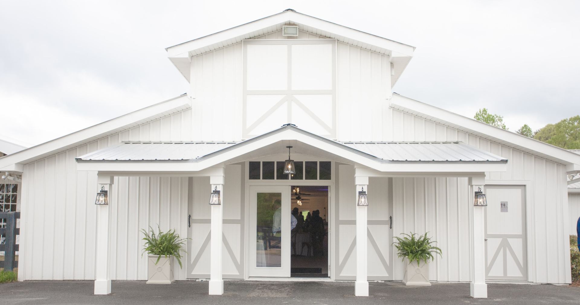 White barn-style building with double doors, covered porch, and potted plants at the entrance