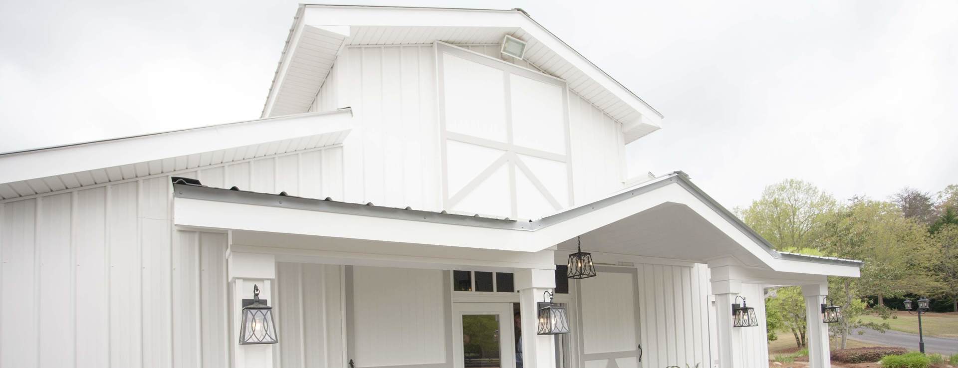 White farmhouse-style building with a front porch, metal roof, and small cupola under a cloudy sky