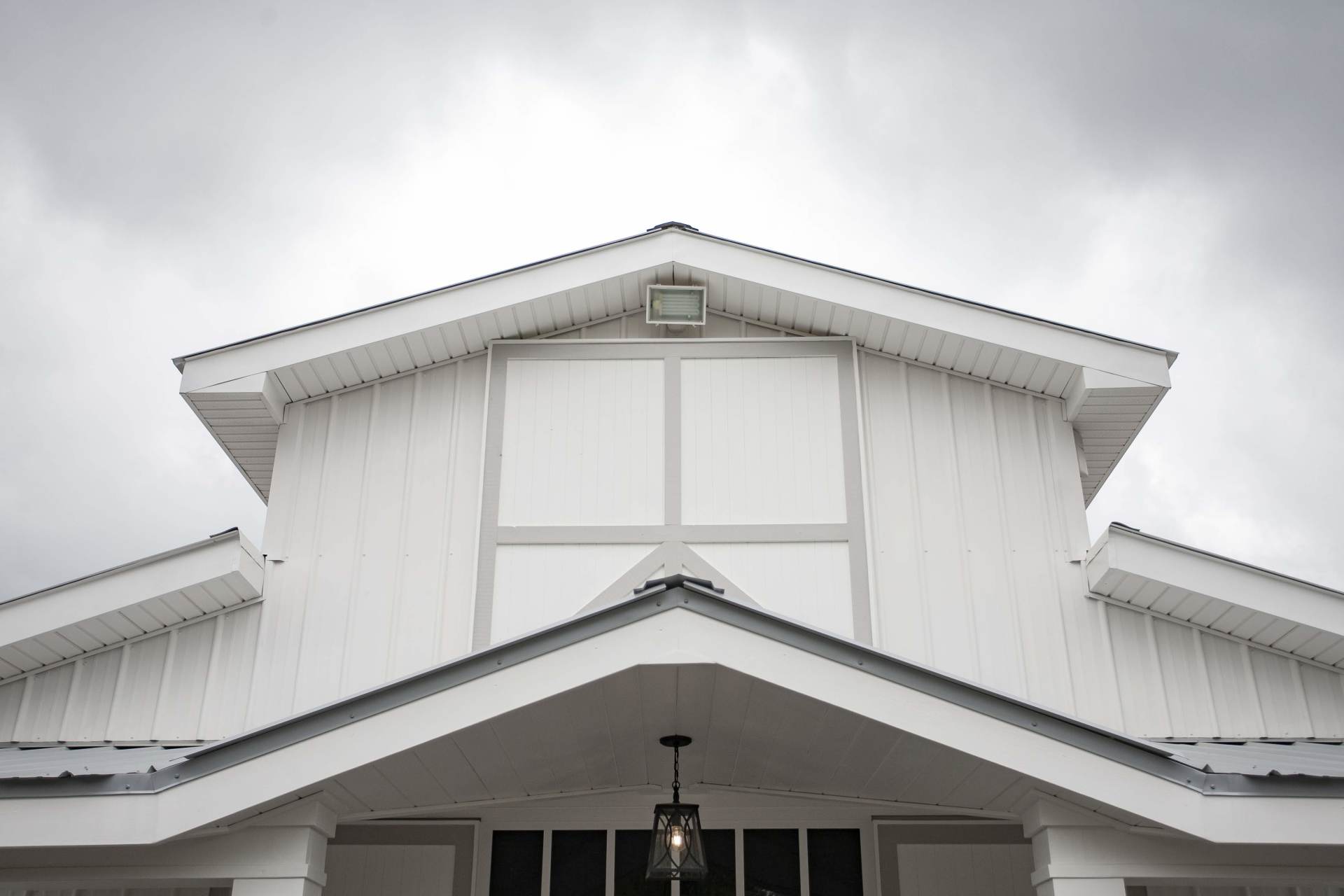 White farmhouse front with gabled roof and porch under a cloudy sky