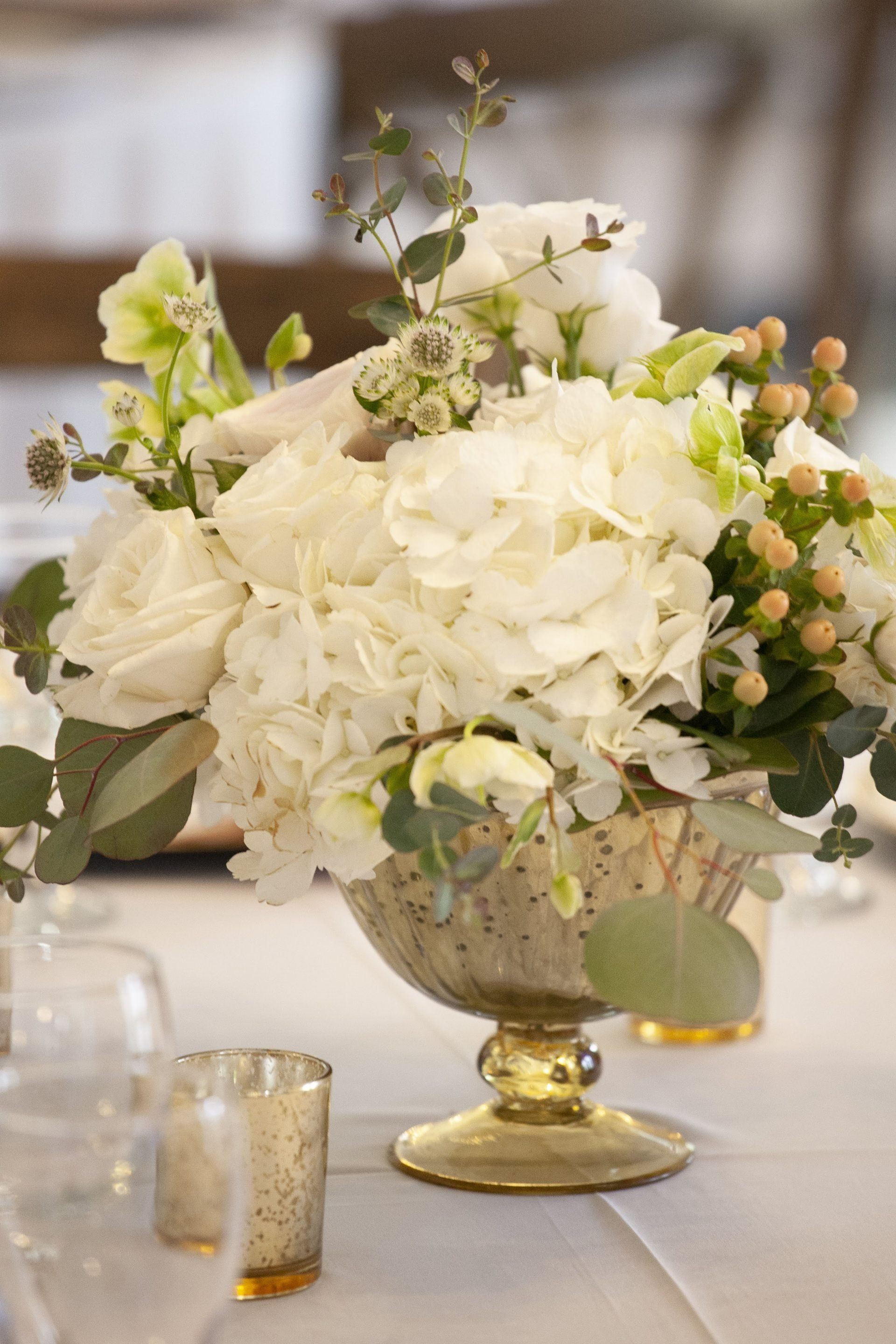 White and pale green floral centerpiece in an ornate gold vase on a table setting
