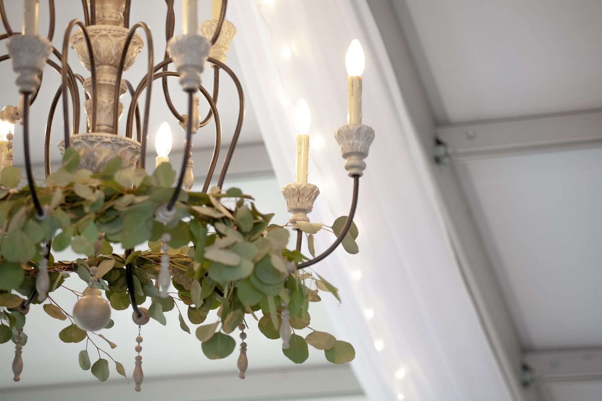 Chandelier with lit bulbs and hanging greenery against a white ceiling