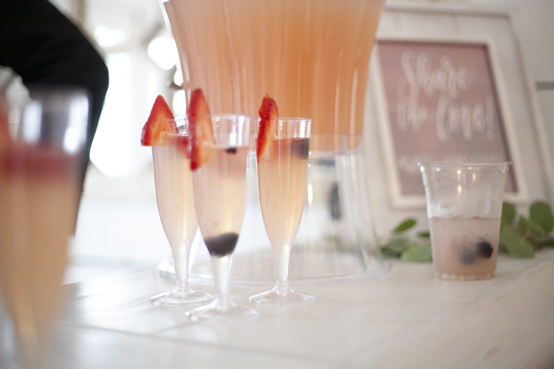 Glasses of orange and berry drinks on a table, with a blurred chalkboard sign in the background
