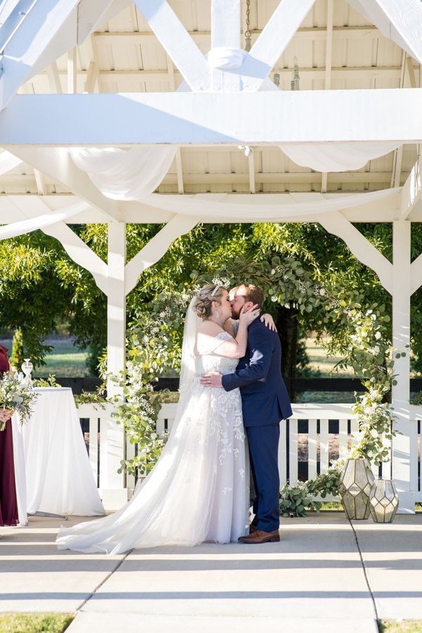 A bride and groom are kissing under a gazebo at their wedding ceremony.