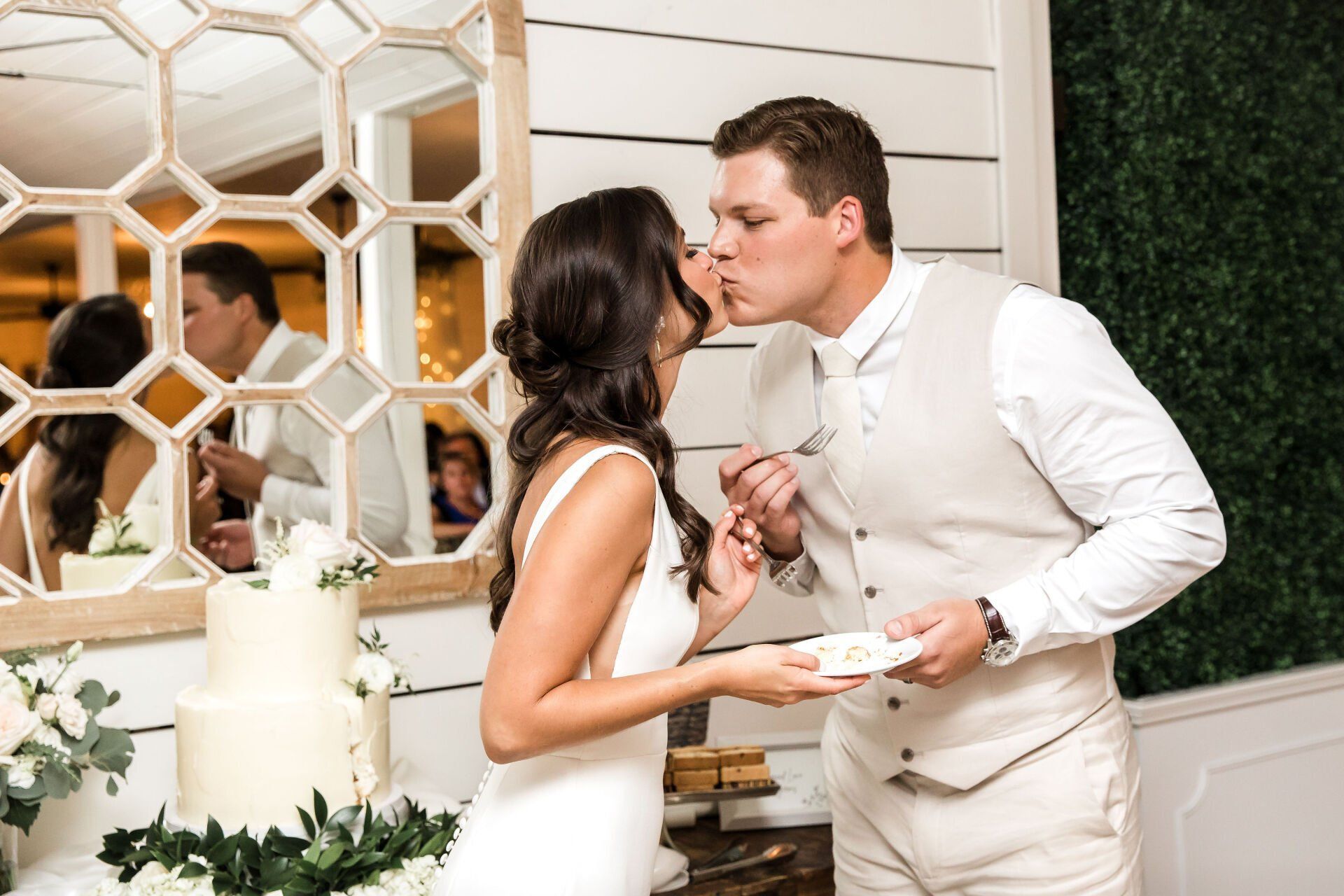 A bride and groom are kissing while cutting their wedding cake.