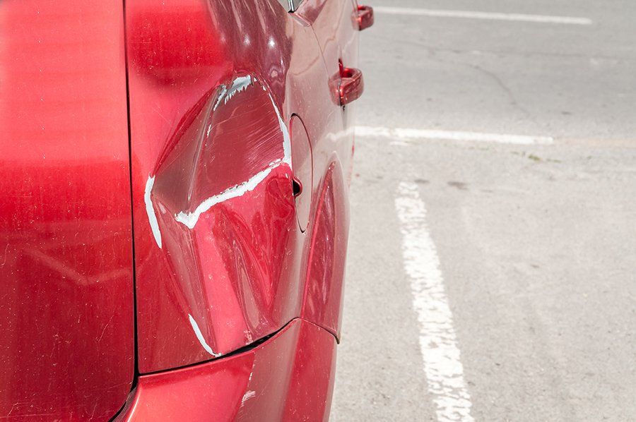 A red car with a damaged fender is parked in a parking lot.