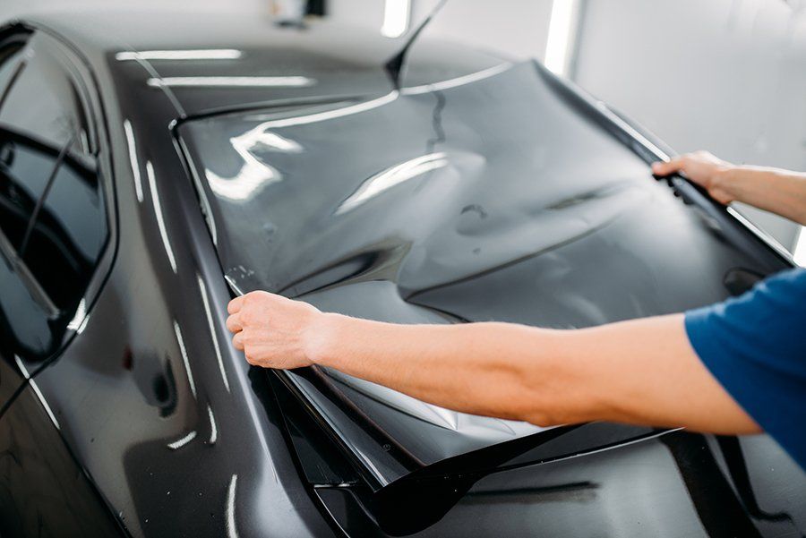 A man is applying window tinting to a black car.
