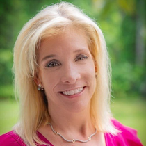 A woman wearing a pink shirt and a necklace is smiling for the camera.