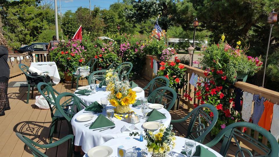 Tables and chairs are set up on a deck with flowers in the background.
