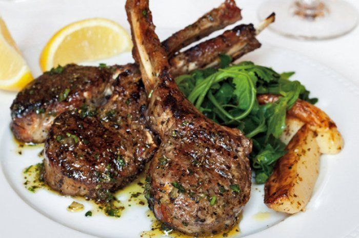 A white plate topped with lamb chops and potatoes
