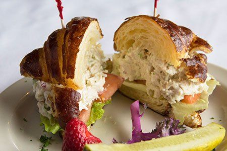 A sandwich on a croissant with a pickle on a plate.