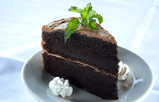 A slice of chocolate cake on a plate with whipped cream and mint leaves