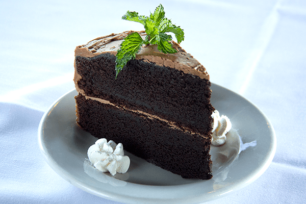 A slice of chocolate cake on a white plate with whipped cream