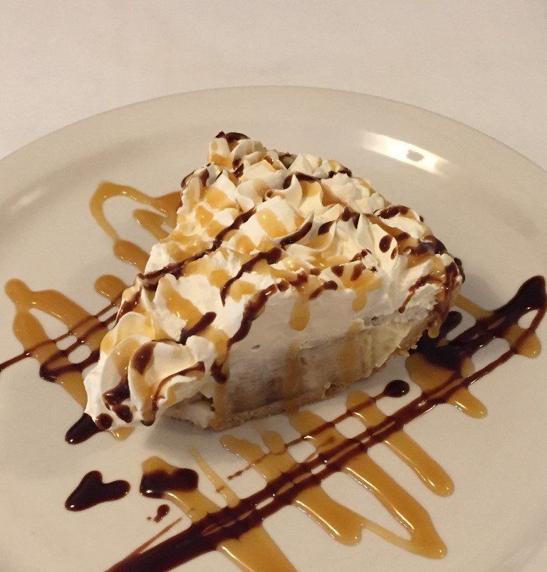 A piece of pie with whipped cream and caramel sauce on a white plate