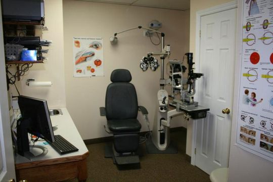 Interior of an optometrist's exam room, with chair, equipment, and eye charts on the walls.