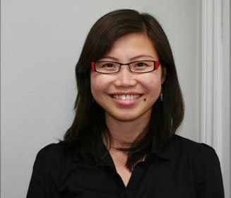 Woman with dark hair, glasses, and a black shirt smiling indoors.