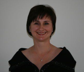 Woman with short dark hair smiles, wearing a black top against a plain wall.