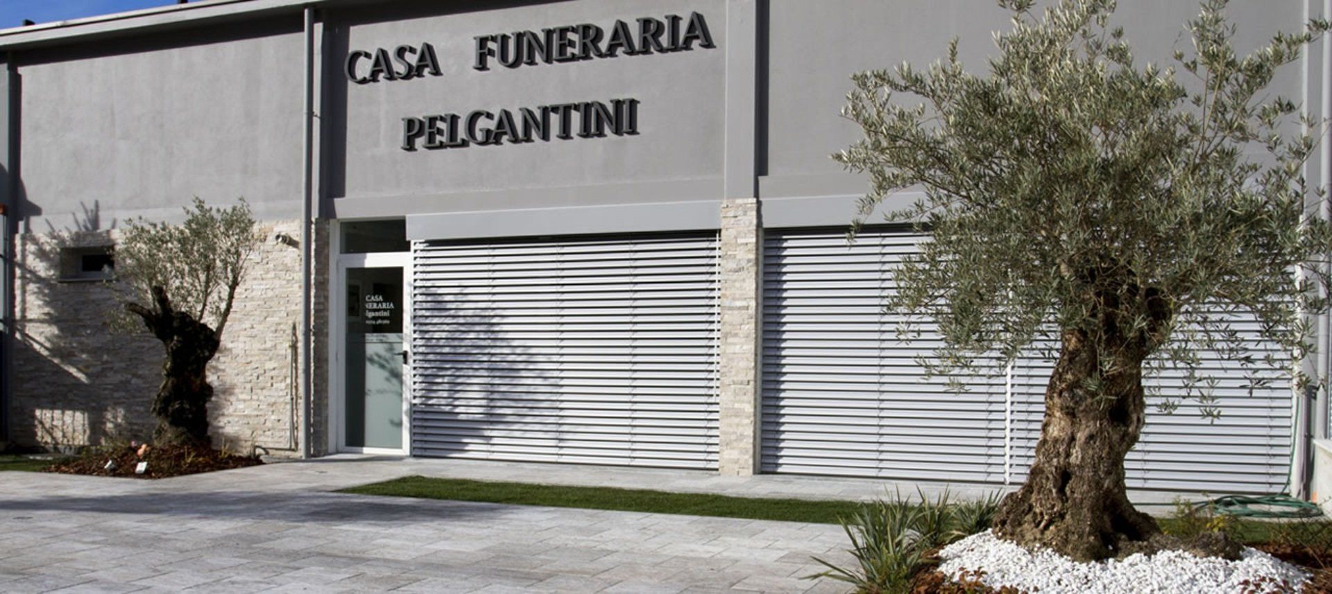 Edificio della Casa Funeraria Pelgantini con alberi e pietra bianca.