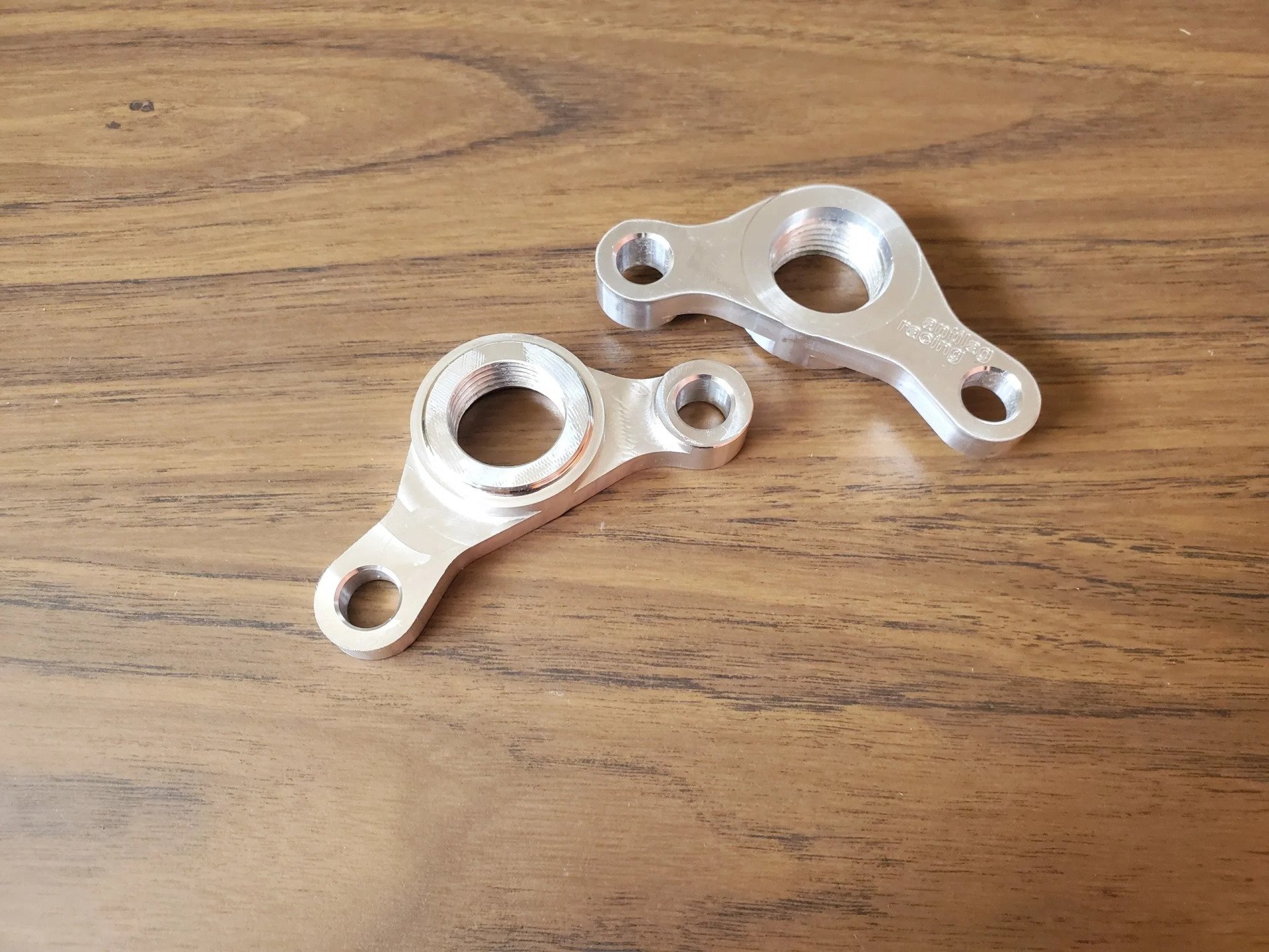 Two metal parts are sitting on a wooden table.