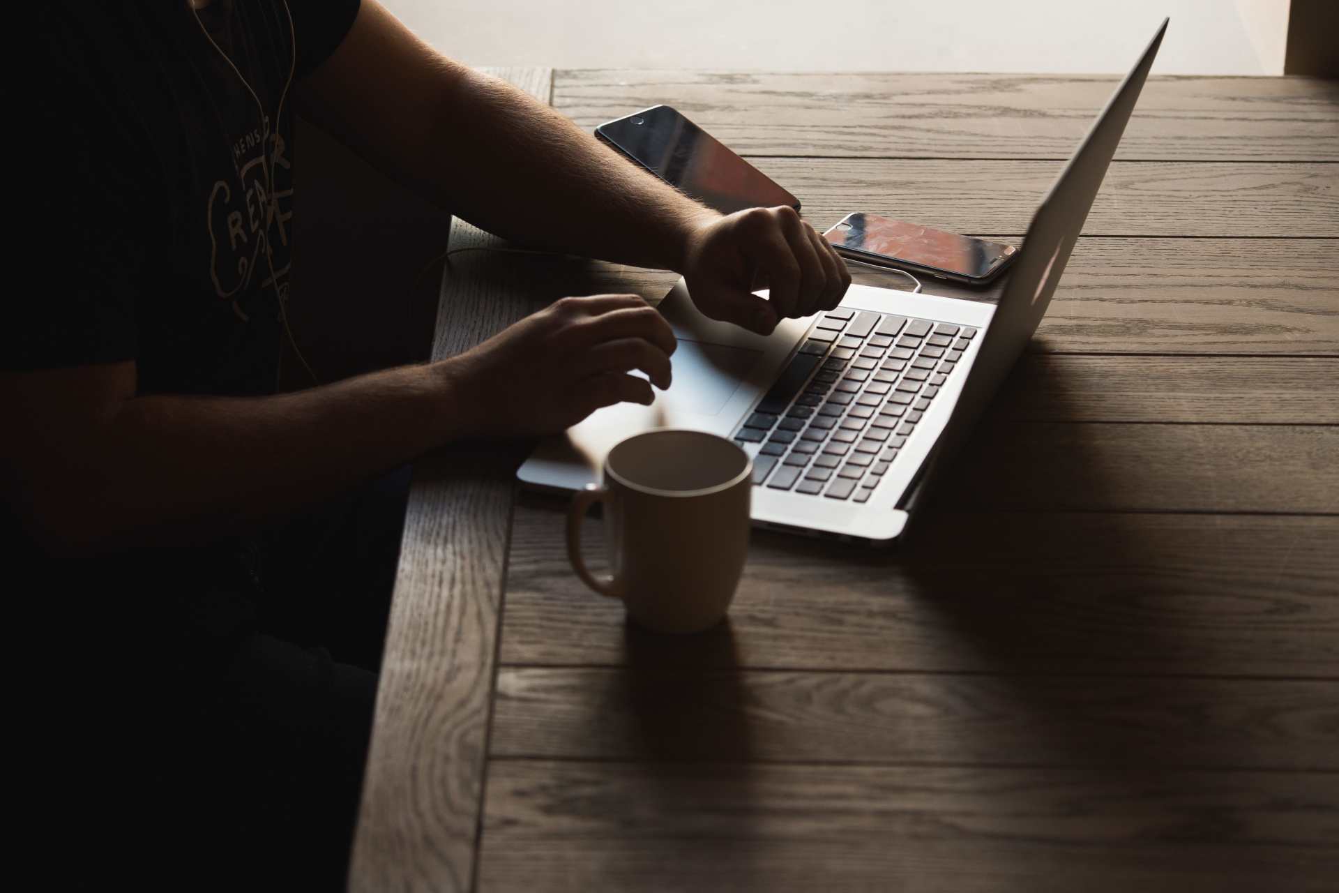 A man is sitting at a wooden table using a laptop computer.