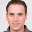 A man in a grey shirt is smiling for the camera.