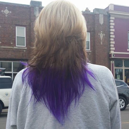 A woman with purple hair is standing in front of a building.