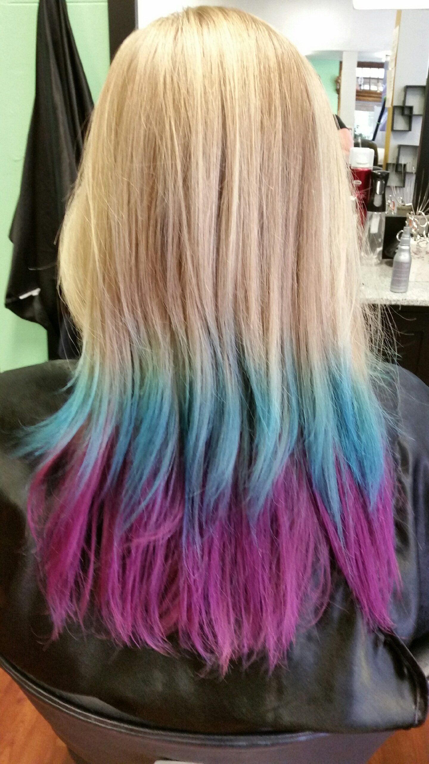 A woman with blonde hair with blue and purple highlights is sitting in a chair.