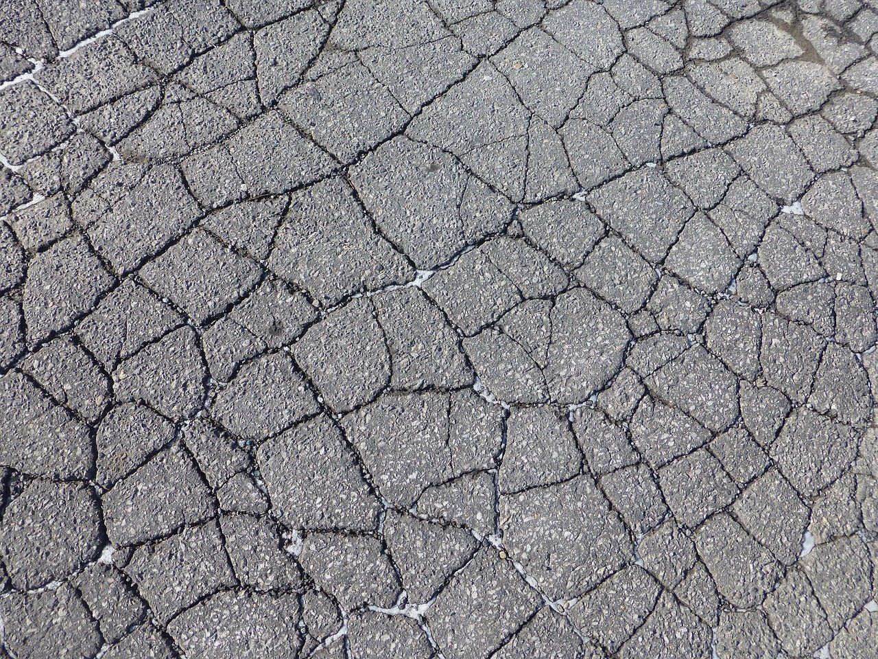 The first image is of a lot of cracked asphalt. The second image is of a bright orange hard hat sitting on an asphalt road.