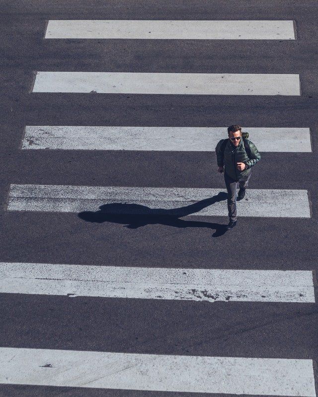 An image of a man wearing a puffy jacket and a backpack running across a crosswalk with thick white lines.