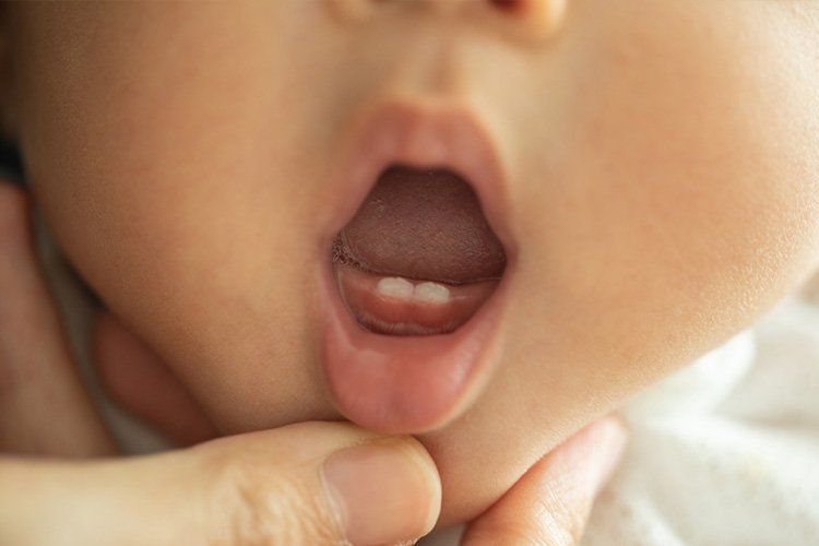 Baby's open mouth, revealing two bottom teeth. A hand is holding the baby's chin.